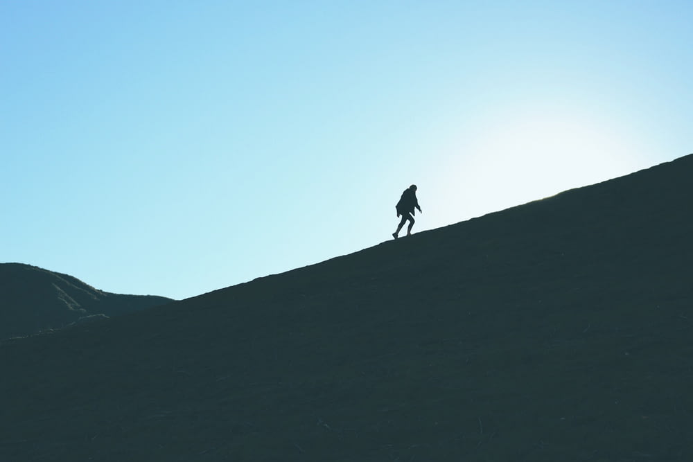 silhouette d’homme escaladant une colline