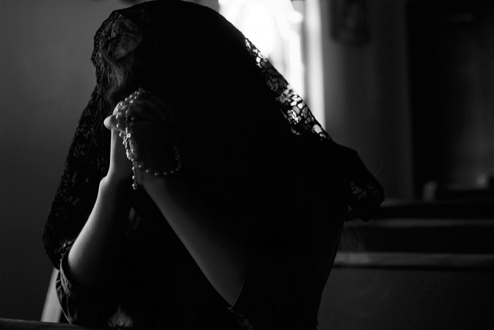 Fotografía en escala de grises de mujer rezando mientras sostiene cuentas de oración