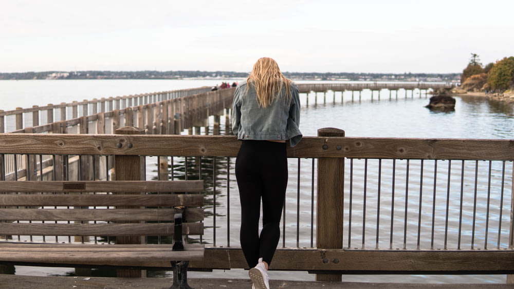 灰色のジャケットと黒いズボンを着た女性が、昼間、茶色の木製の桟橋に立っている