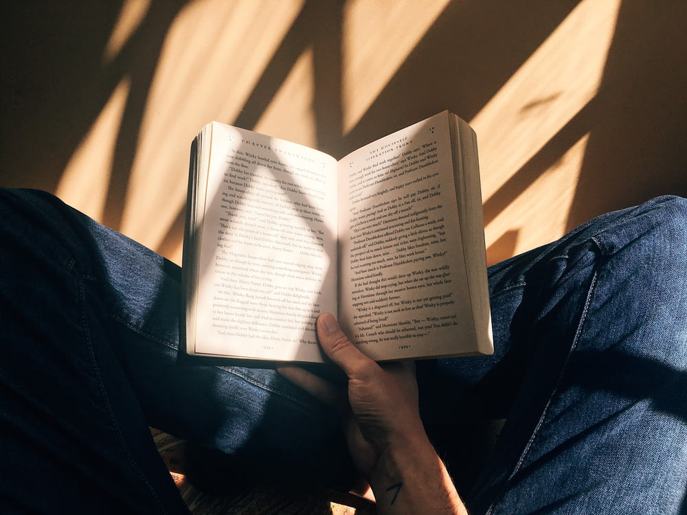 Persona sosteniendo un libro sentado sobre una superficie marrón