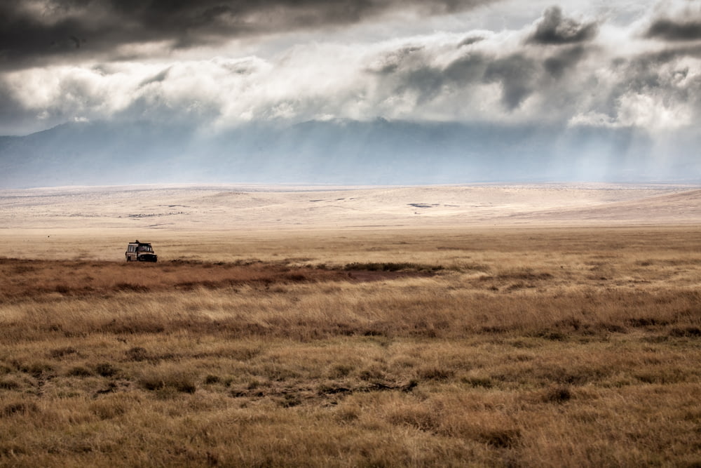 car on brown field under white clouds and blue sky