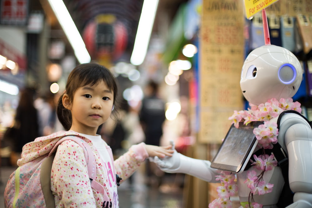 Foto de la niña que pone la mano izquierda en un robot digital blanco