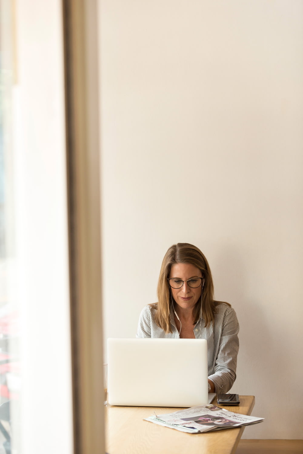 회색 줄무늬 드레스 셔츠를 입은 여자가 흰색 노트북 컴퓨터 앞에서 갈색 나무 테이블 근처에 앉아 있습니다.