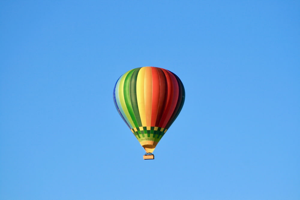 Foto de ángulo bajo de globo aerostático multicolor volando bajo skty azul