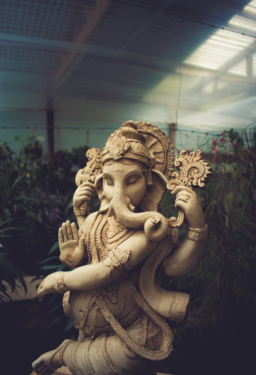estátua de Ganesha de concreto marrom que está atrás das plantas