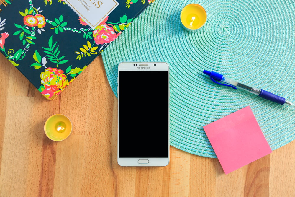 teléfono inteligente Samsung Galaxy blanco en la parte superior del mantel individual azul cerca del bolígrafo de clic azul