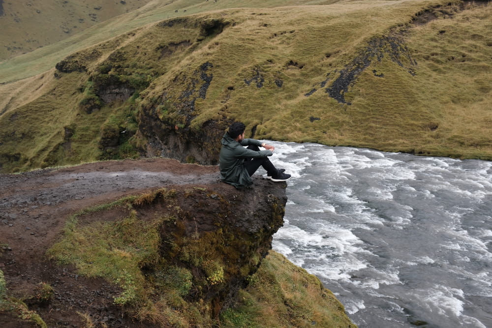 man sit on mountain near body of water
