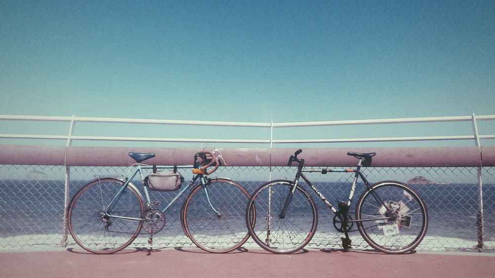 two black and gray bicycles parked near fence on seashore at daytime