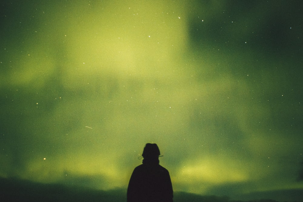 Persona in piedi sotto l'aurora boreale verde