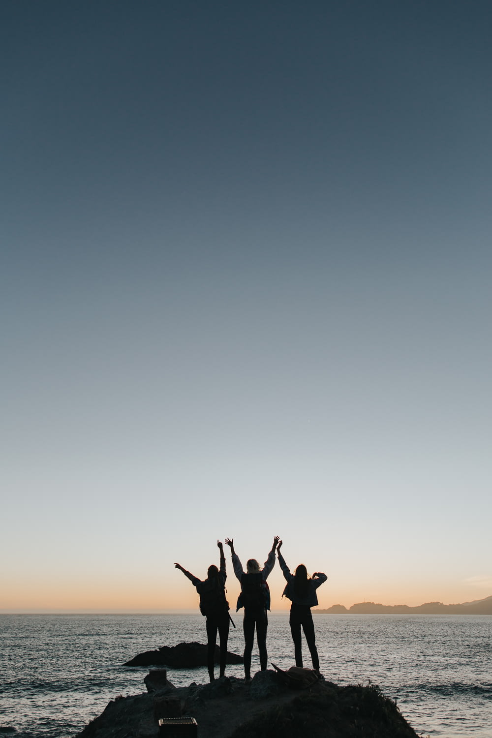 Silhouettenfotografie von Personen, die die Hände heben, während sie auf der Insel stehen