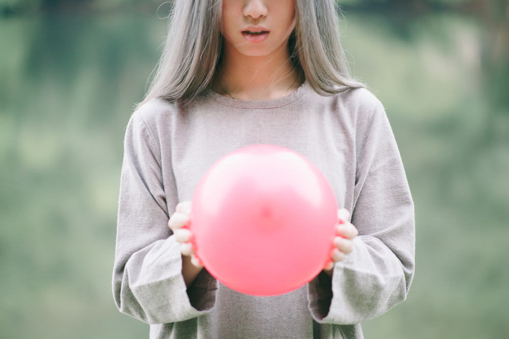 fille en chemise grise à manches longues tenant un ballon rose