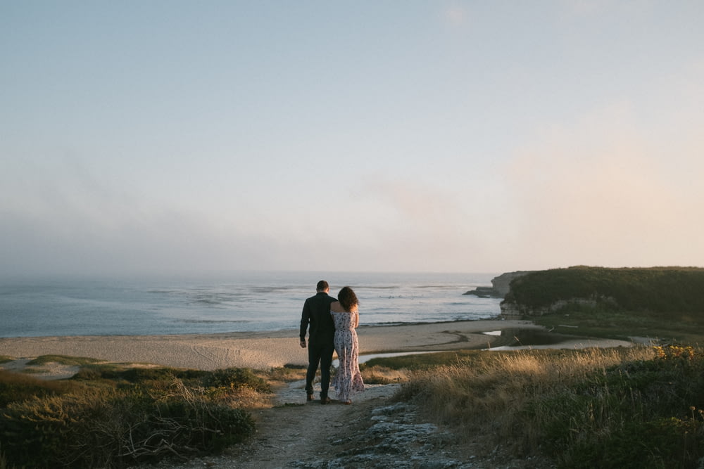 a man and woman standing on a path near the ocean
