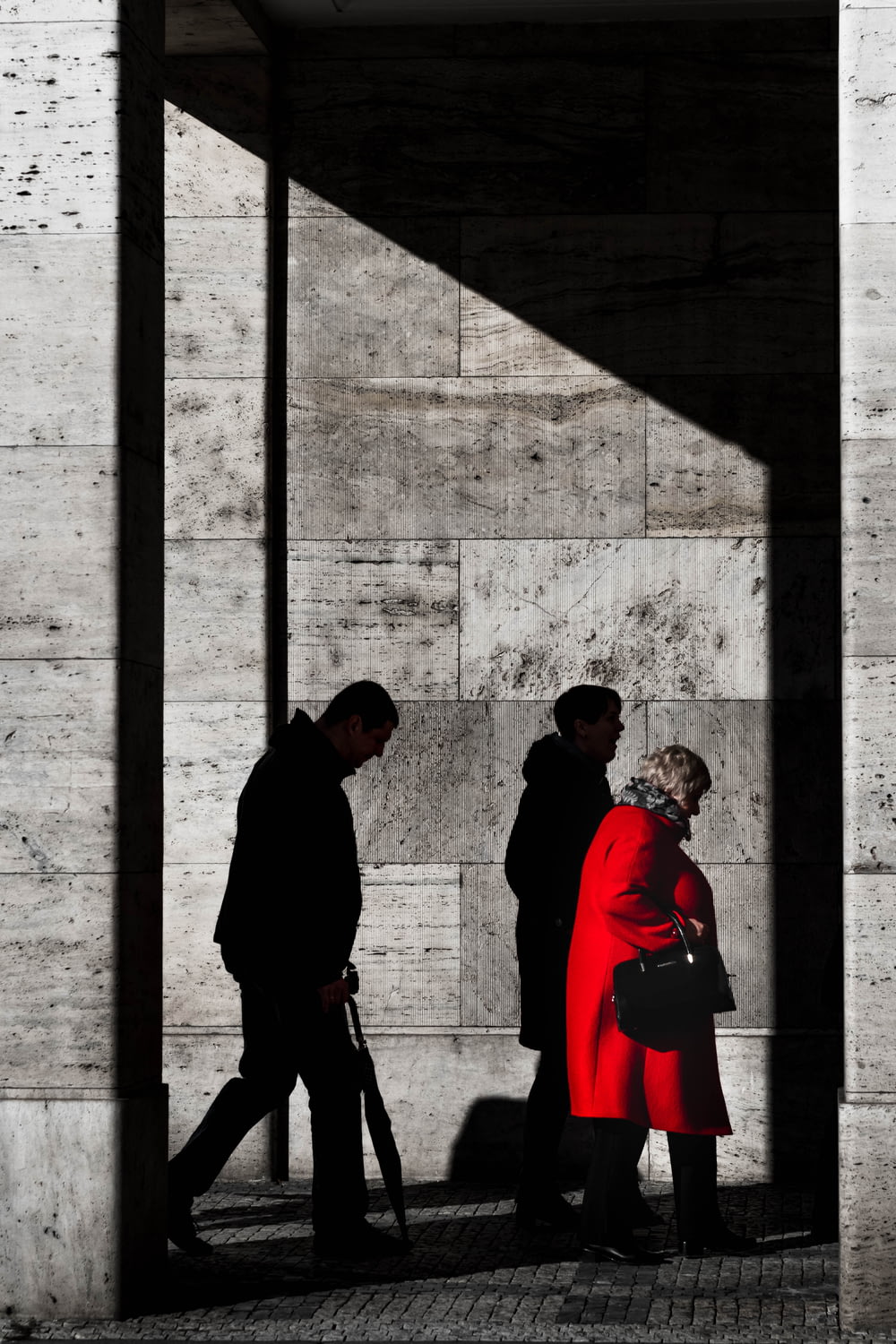 two men and woman walking beside gray concrete wall with sahdow