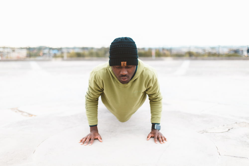man in green long-sleeved shirt doing a push-up on gray concrete pavement