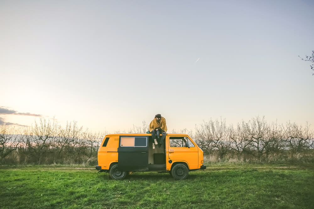 Persona sentada en la parte superior de una furgoneta amarilla en el campo de hierba durante el día