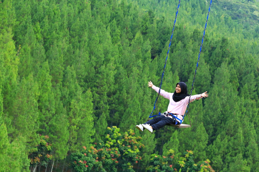 woman with open arms riding swing above green trees at daytime