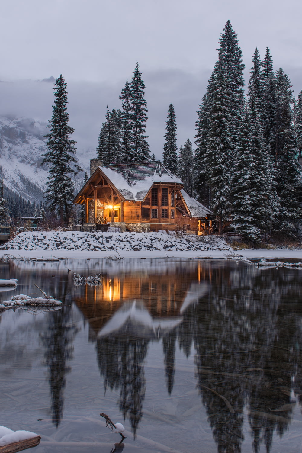 Maison en bois près des pins et de l’étang recouvert de neige pendant la journée