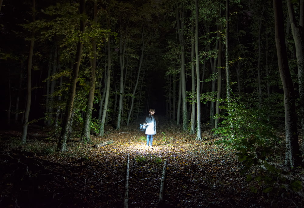 woman standing holding flashlight into woods