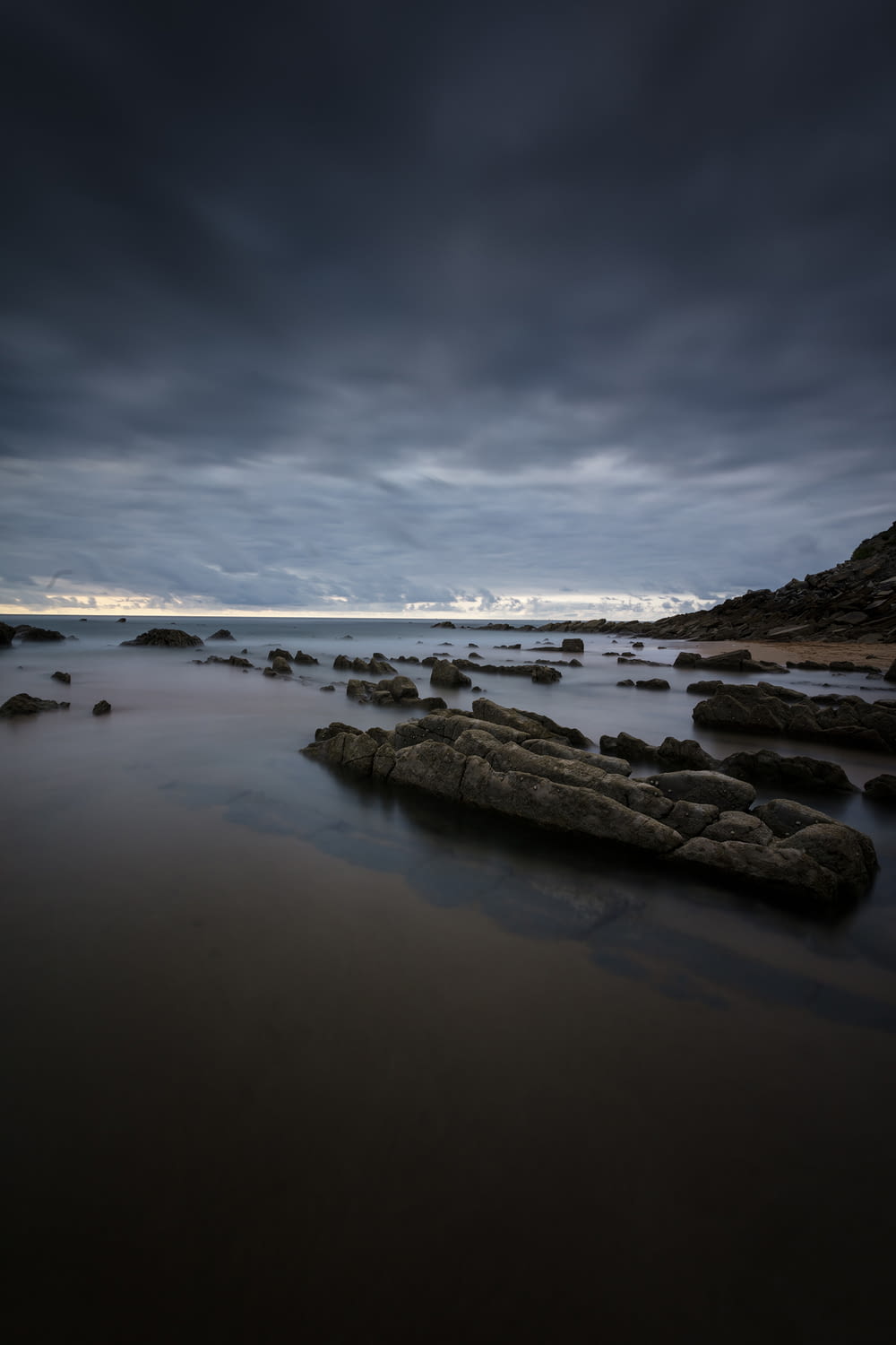 Formation rocheuse noire sur un plan d’eau calme sous des nuages gris