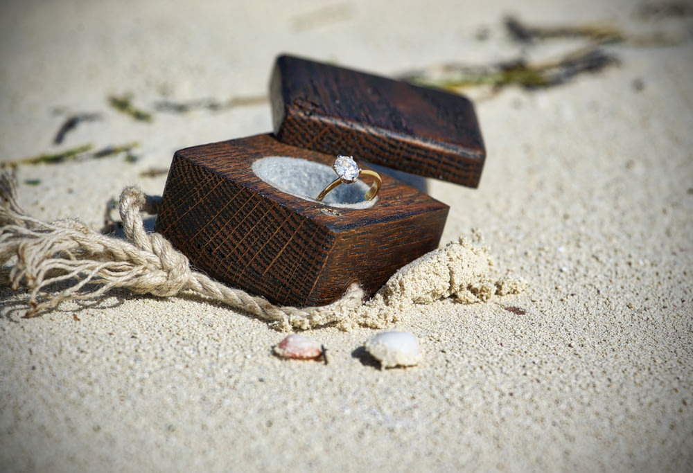 anello con pietre preziose trasparenti color oro in scatola di legno marrone su sabbia