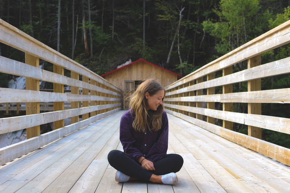 woman sitting on wooden bridge near forest