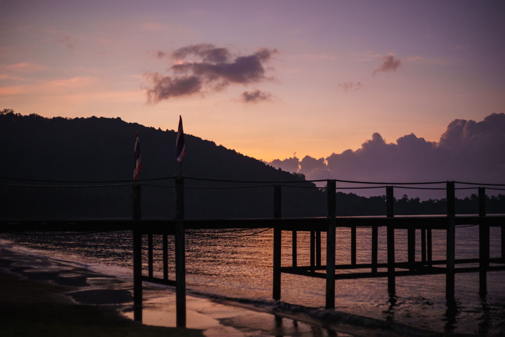 silhouette of wooden dock near mountain beside body of water during sunset