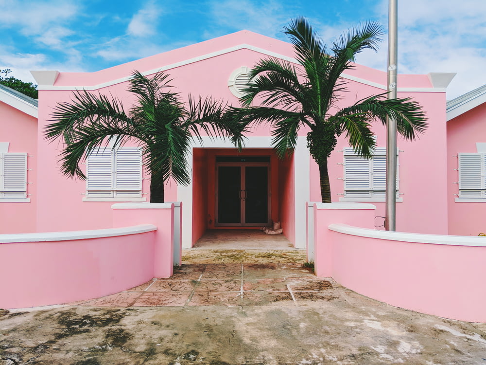 흐린 하늘 아래 푸른 나무 근처의 분홍색과 흰색 콘크리트 집