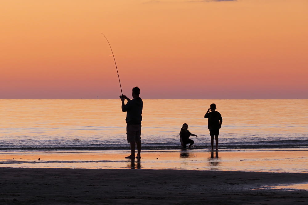 silhouette photo of a man fishing near shore during golden time