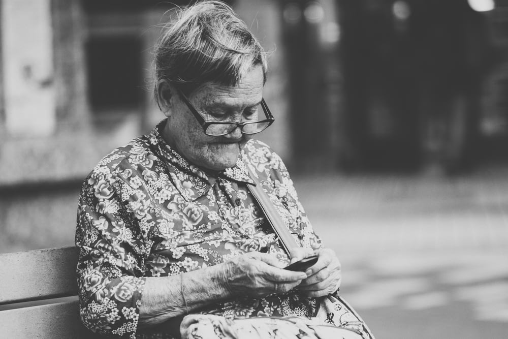 selective focus grayscale photography of woman using phone while sitting at bench