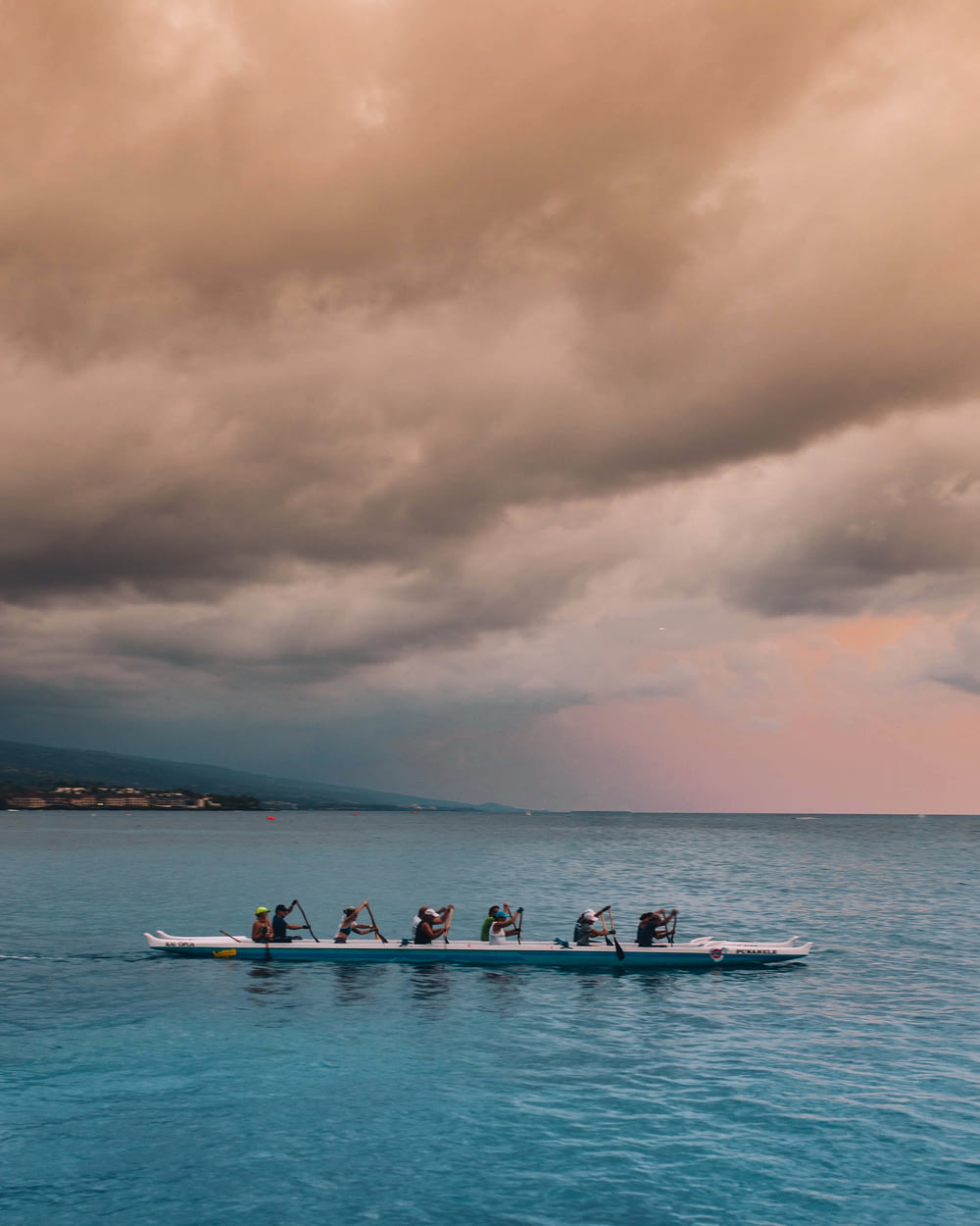 Persone sulla barca bianca e blu che remano sotto le nuvole grigie durante il giorno