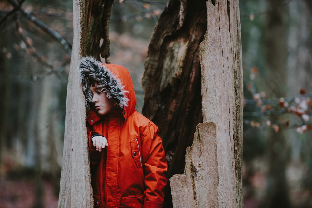 person wearing parka leaning on dead tree during daytime