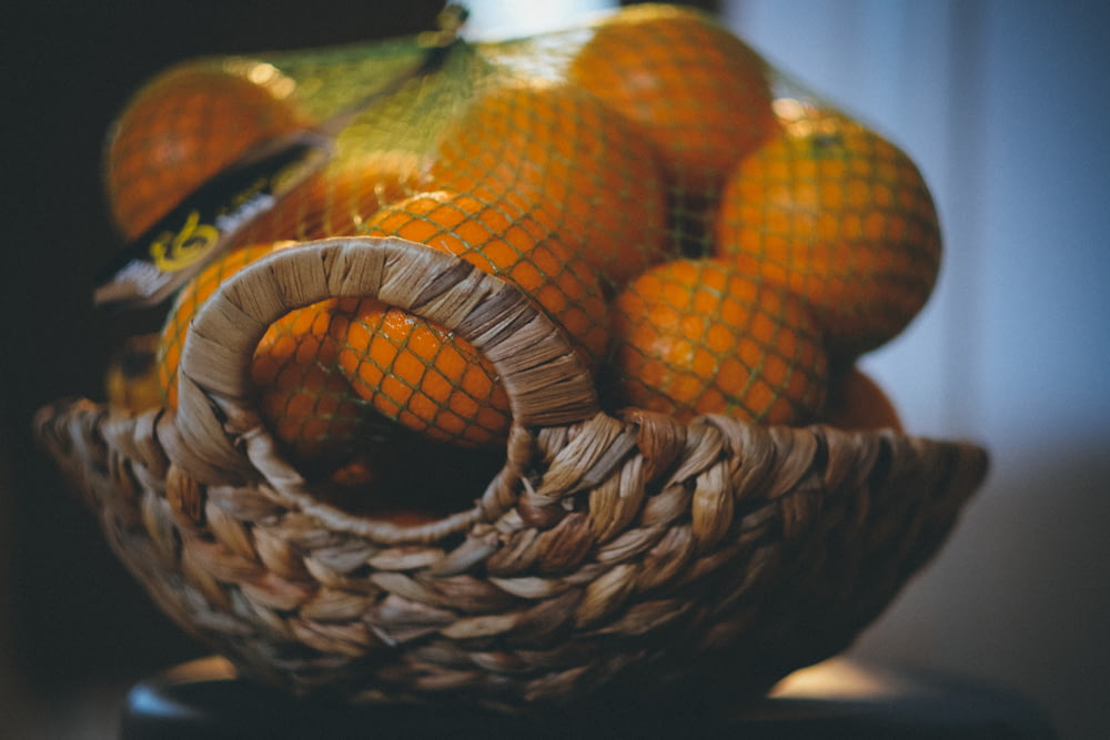 Selektives Fokusfoto einer Traube orangefarbener Früchte im braunen Weidenkorb