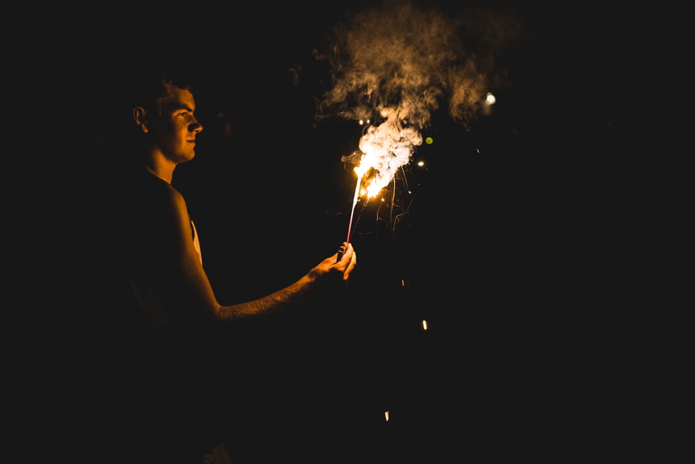a man holding a lit sparkler in the dark