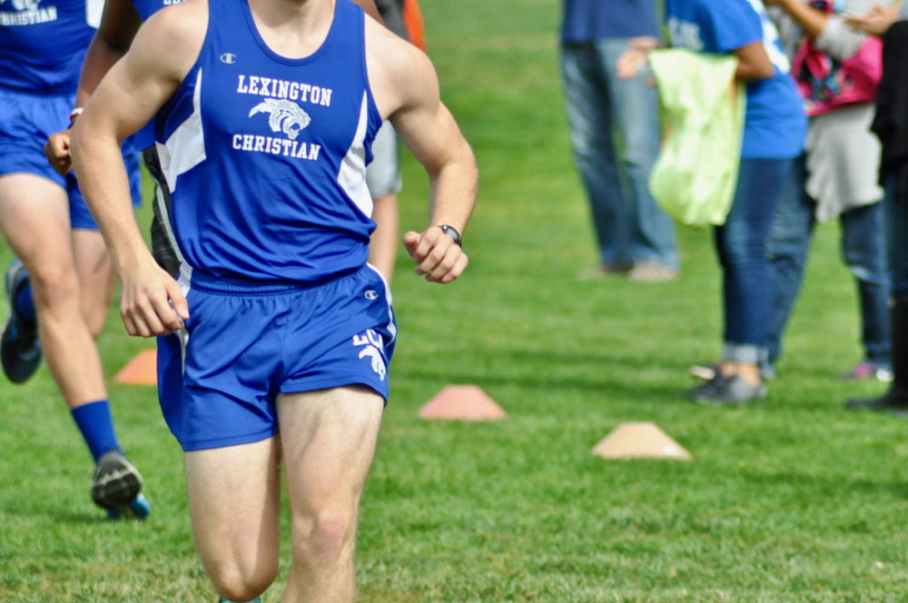 man in blue Champion tank top and shorts running at the field