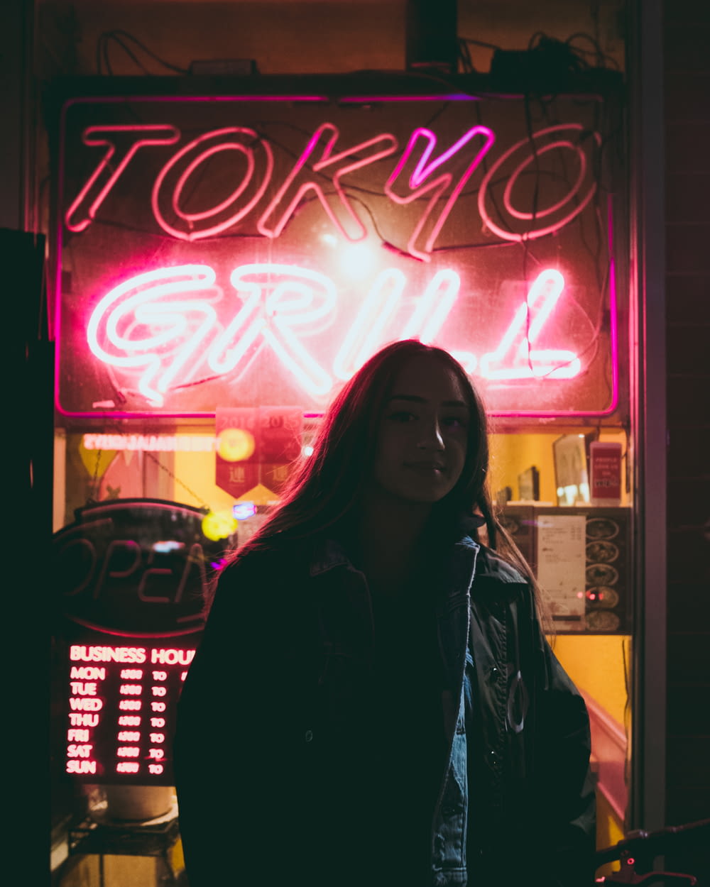 mujer de pie detrás de la señalización de neón roja de Tokyo Grill