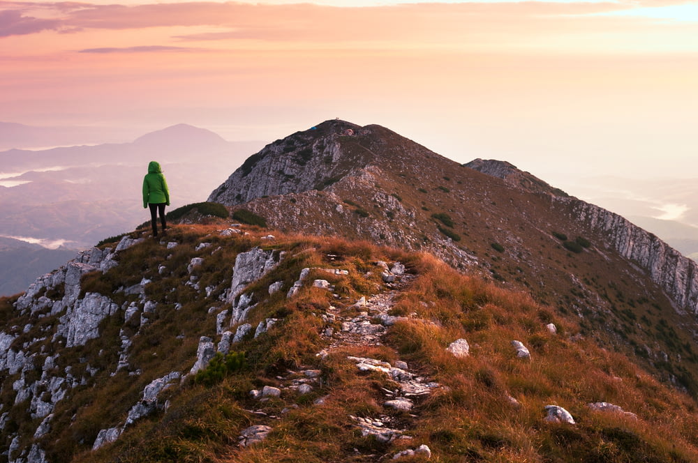 Person mit grüner Jacke, die auf einer Klippe mit Blick auf den Berg steht