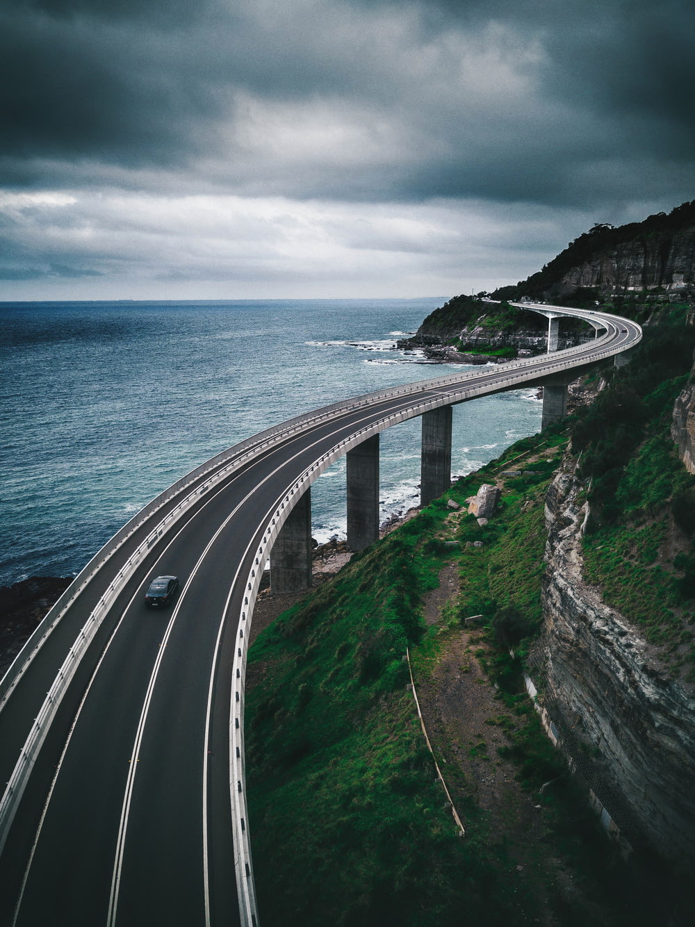 ponte rodoviária de concreto cinza perto da colina e do oceano sob o céu branco e azul