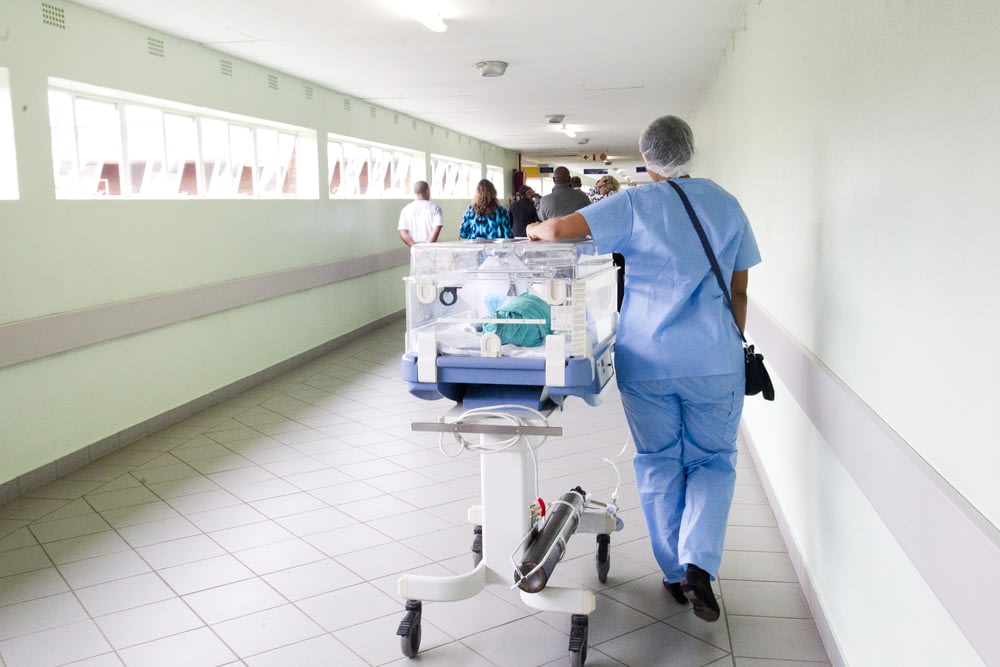 Persona caminando por el pasillo en traje médico azul cerca de la incubadora