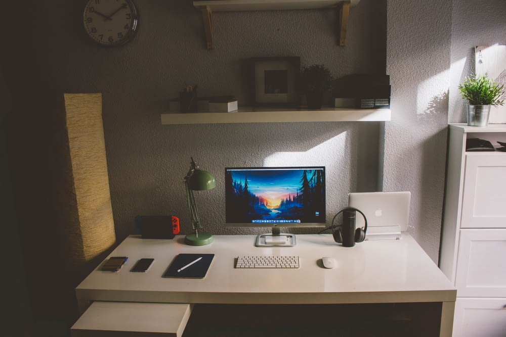 silberner iMac und weiße kabellose Tastatur auf weißem Holztisch im Zimmer