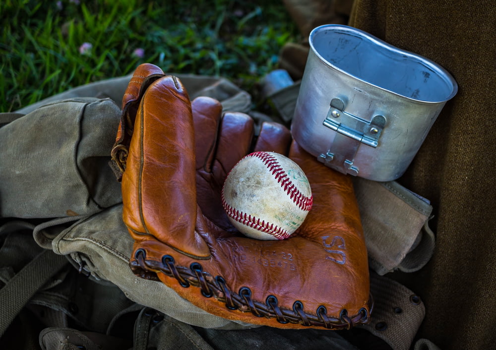 Guante de béisbol de cuero marrón con pelota de béisbol junto a contenedor gris y textil marrón durante el día