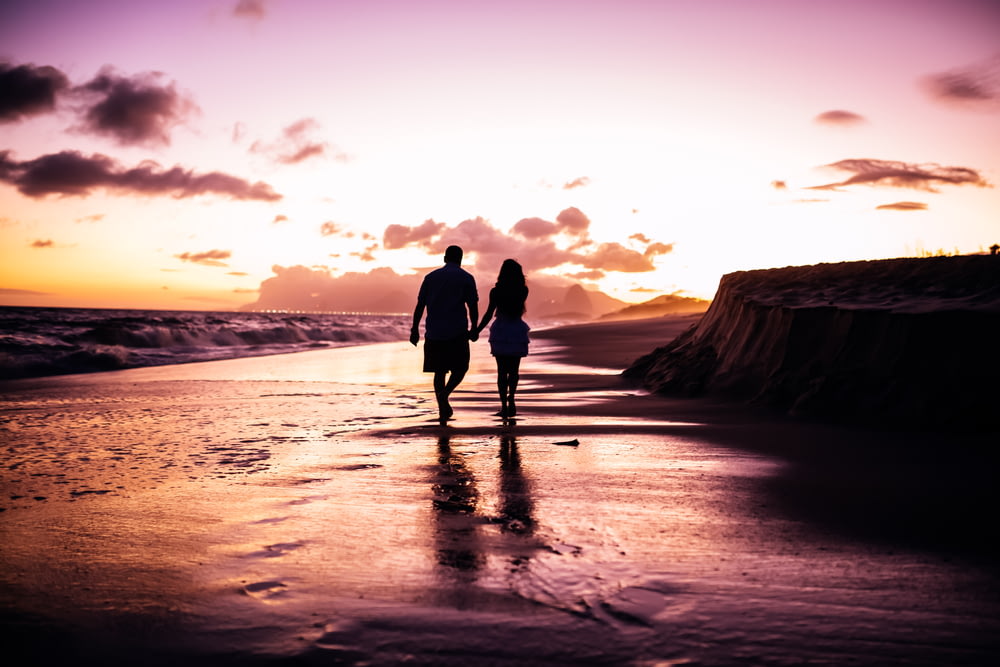 couple holding hands while walking on shore