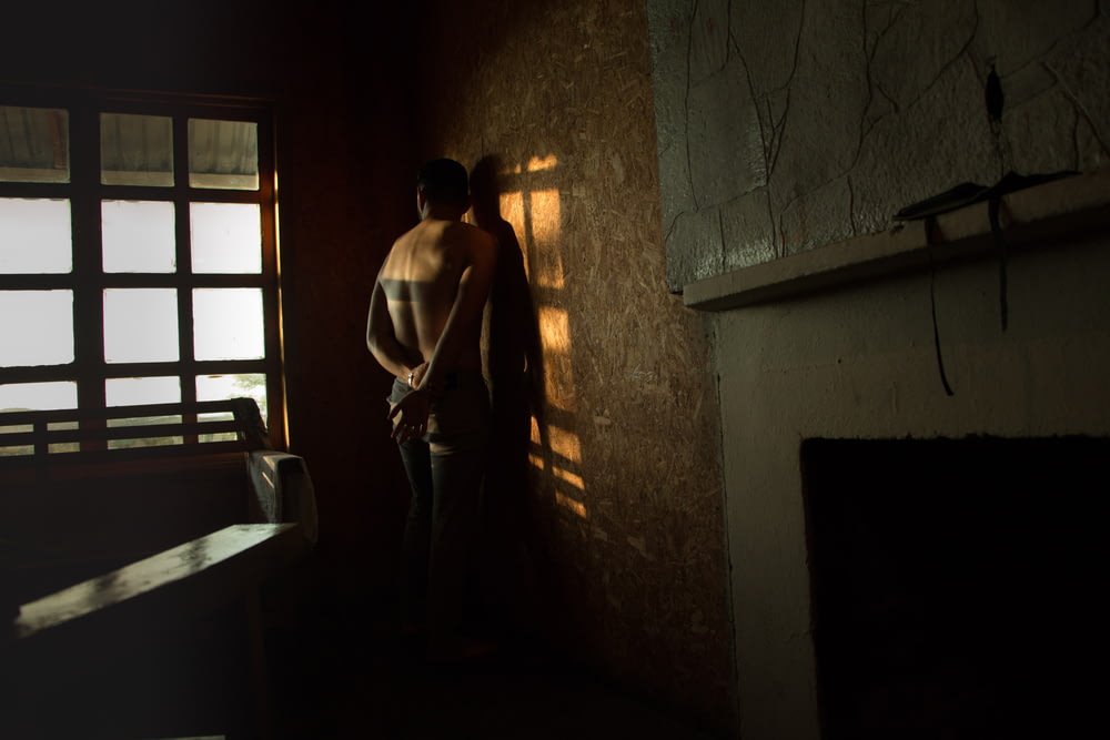 hombre en topless frente a la pared al lado de la cama dentro de la habitación