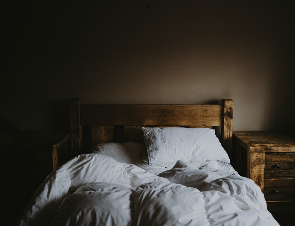 Juego de edredón de cama blanco y estructura de cama de madera marrón junto a mesita de noche de madera marrón