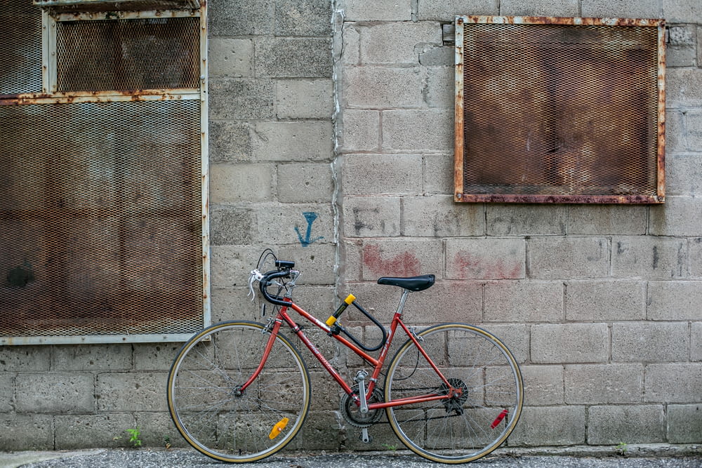 red and black drop-handled road bike leaning on gray concrete wall during daytime