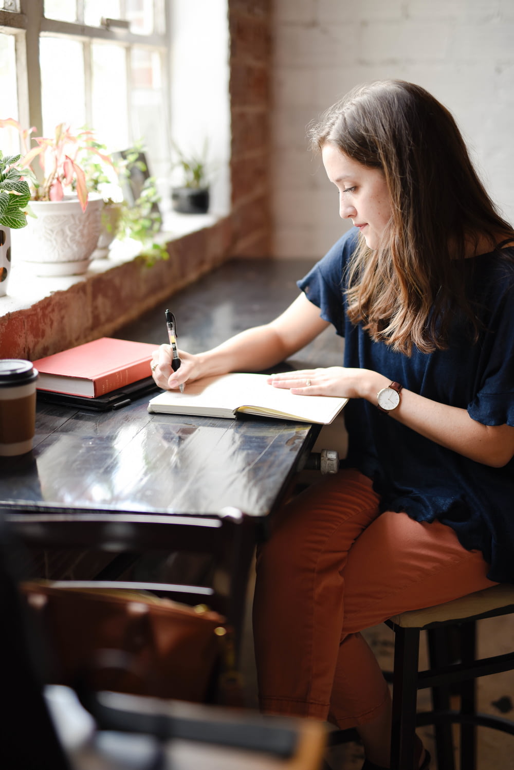 창가 근처의 흰 책에 글을 쓰는 검은 테이블 앞에 앉아있는 여자