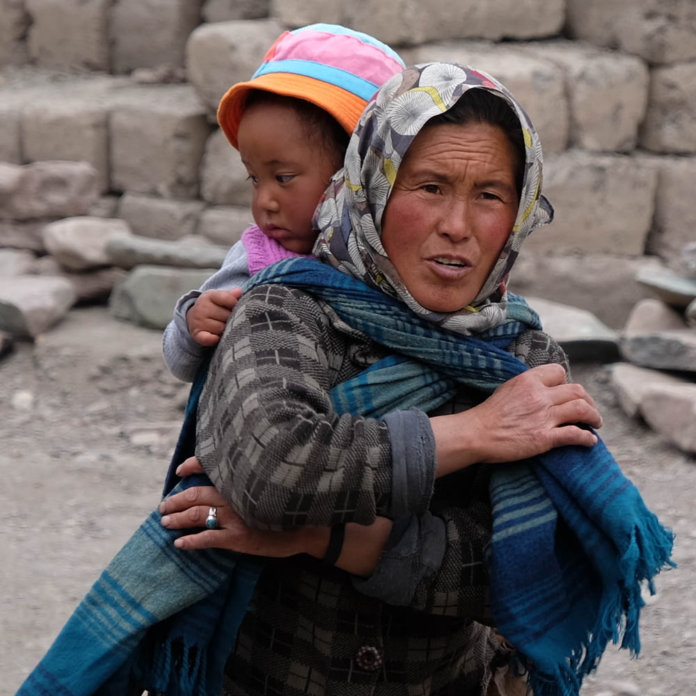 woman wearing scarf while carrying a girl at her back during daytime