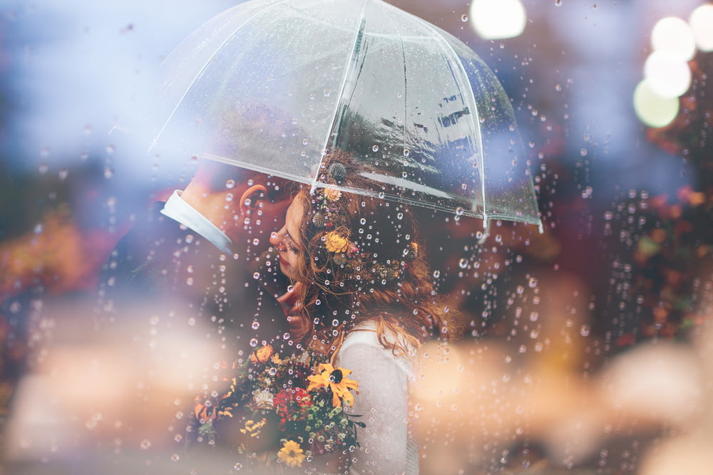 雨の中、傘の下でキスをする新郎新婦