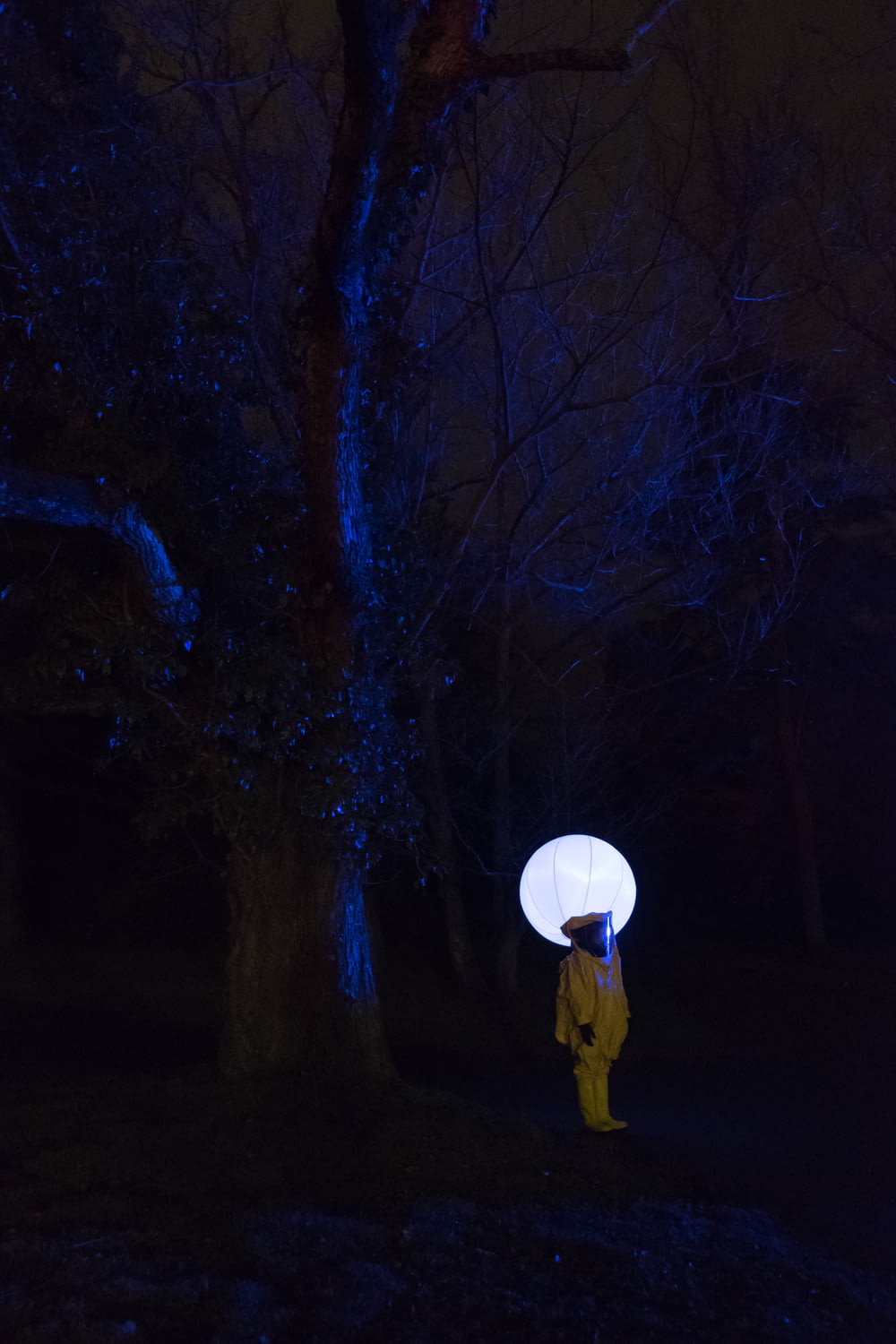 Person im weißen Outfit, die nachts unter einem blattlosen Baum steht