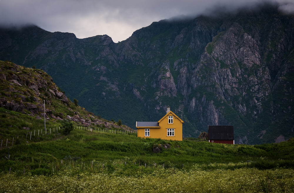 Casa de madeira amarela perto da montanha durante o dia nublado