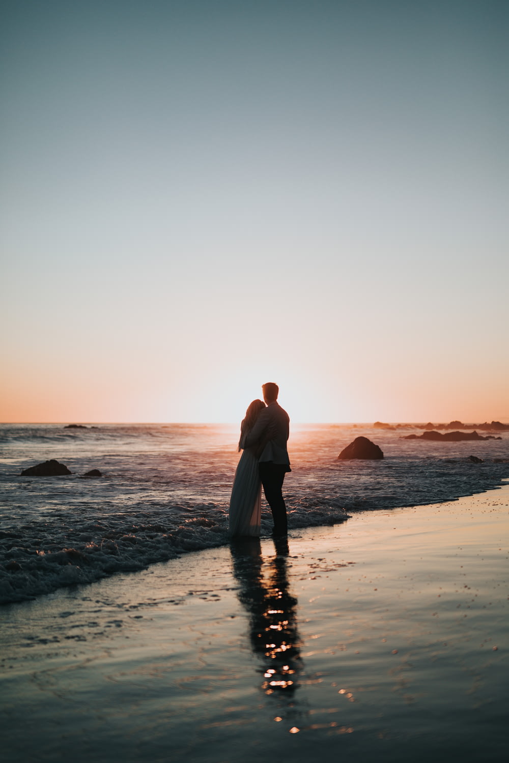 Foto de la silueta de la pareja de pie en la playa viendo la puesta del sol